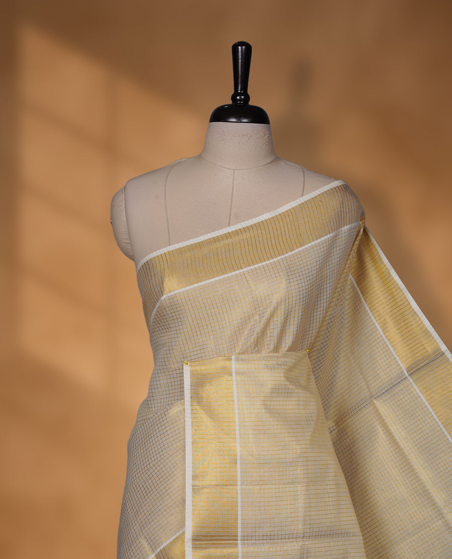 Off-white colour tissue Kerala saree with a subtle gold-toned checkered body, finished with a classic gold kasavu border along the edges and pallu, paired with a matching blouse.