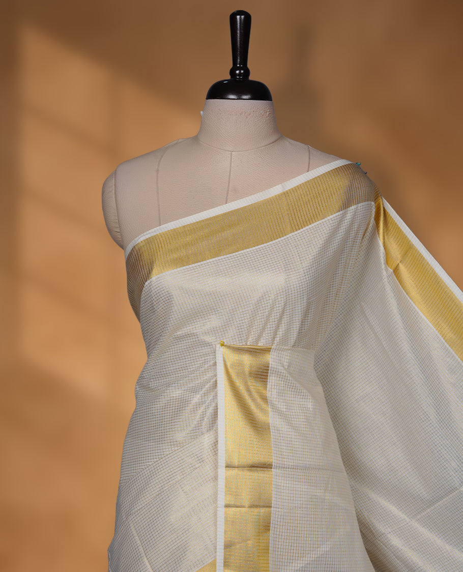 Elegant off-white colour cotton Kerala saree, highlighted with a classic gold kasavu border and subtle woven checks across the body. Finished with a clean, traditional pallu with a coordinating blouse.
