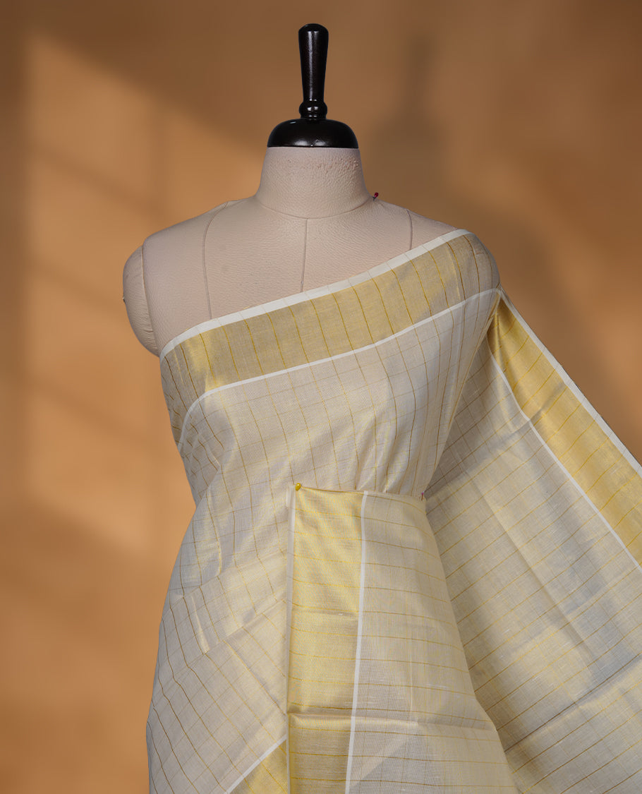 Off-white colour tissue Kerala saree with subtle gold checks across the body, finished with a traditional striped gold kasavu border and delicate tassel detailing on the pallu, paired with a matching blouse.
