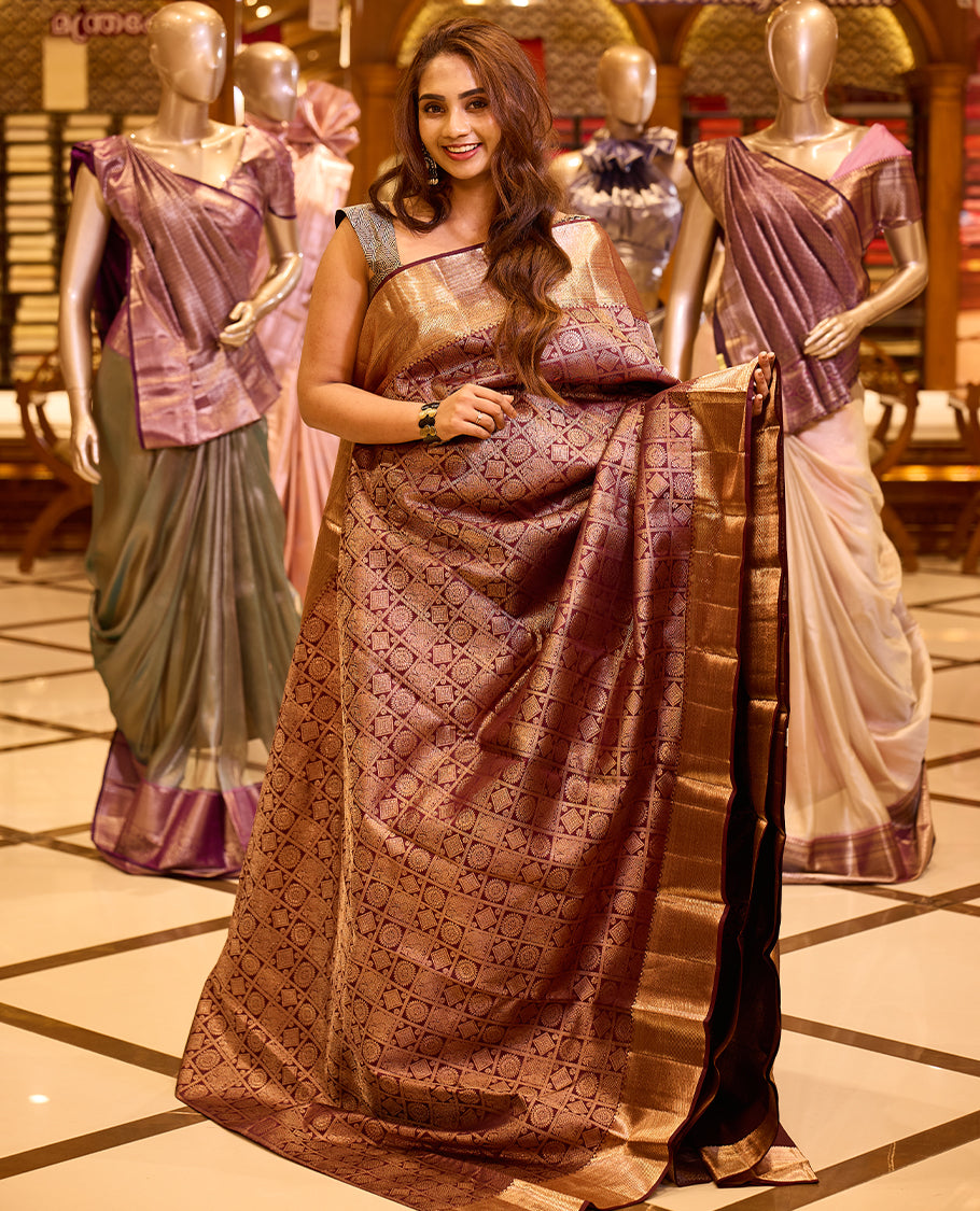 Elegant wine brown colour Kancheepuram silk saree adorned with an all over rich geometric zari weave, beautifully complemented by a broad traditional gold zari border and paired with a matching blouse piece