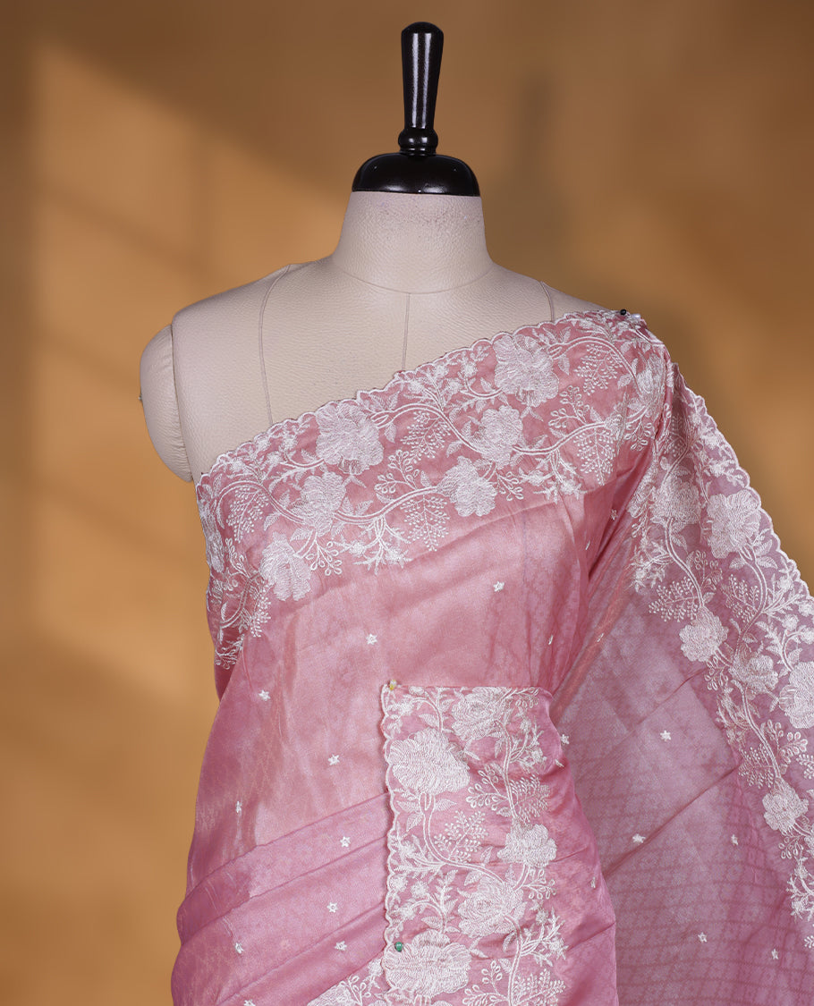 Pink colour organza designer saree featuring a subtle self patterned body and an intricately scalloped floral thread embroidered border all around, complemented by a coordinating embroidered pallu and paired with a matching blouse.