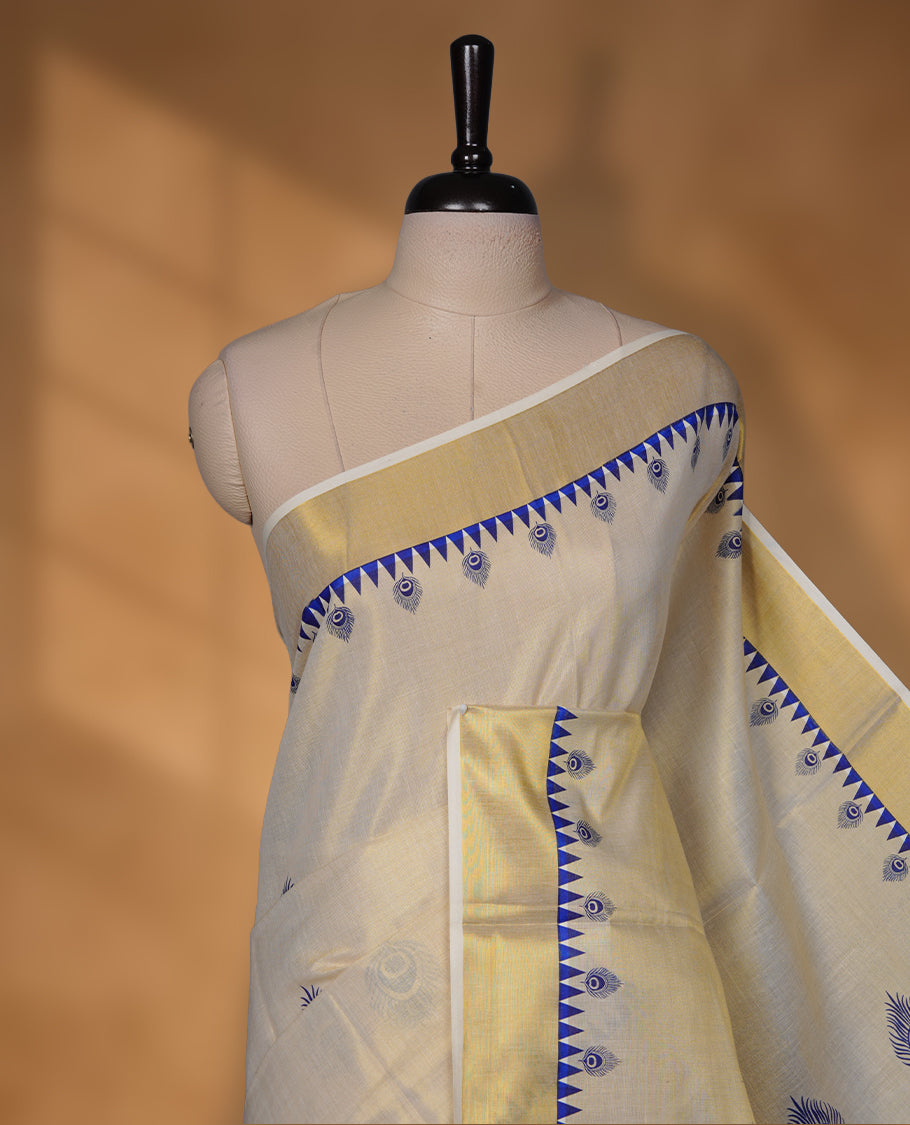 Off-white colour tissue Kerala saree with a classic gold kasavu border, highlighted by royal blue peacock motifs across the body and pallu, and paired with a matching blouse.
