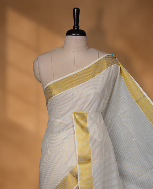 Off-white colour cotton Kerala saree featuring a traditional gold kasavu border with a fine striped texture across the body and pallu, offering a clean, elegant look, and paired with a matching blouse.