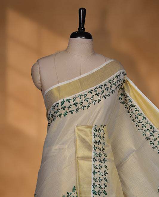 Off-white colour tissue Kerala saree featuring a classic gold kasavu border, highlighted with elegant green leafy and floral motifs across the body and pallu, and paired with a matching blouse.