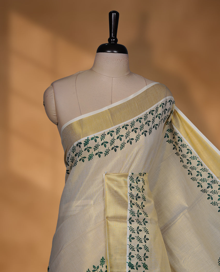Off-white colour tissue Kerala saree featuring a classic gold kasavu border, highlighted with elegant green leafy and floral motifs across the body and pallu, and paired with a matching blouse.