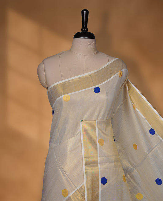 Off-white colour Tissue Kerala saree featuring playful blue and gold polka buttas across the body, finished with a classic gold kasavu border and paired with a matching blouse.