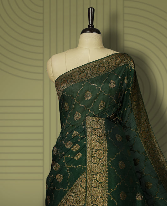 Dark green colour semi Banarasi Tussar Georgette saree with gold zari motifs on the body, a grand woven golden pallu, and ornate zari border. Includes a matching blouse piece for a complete look.