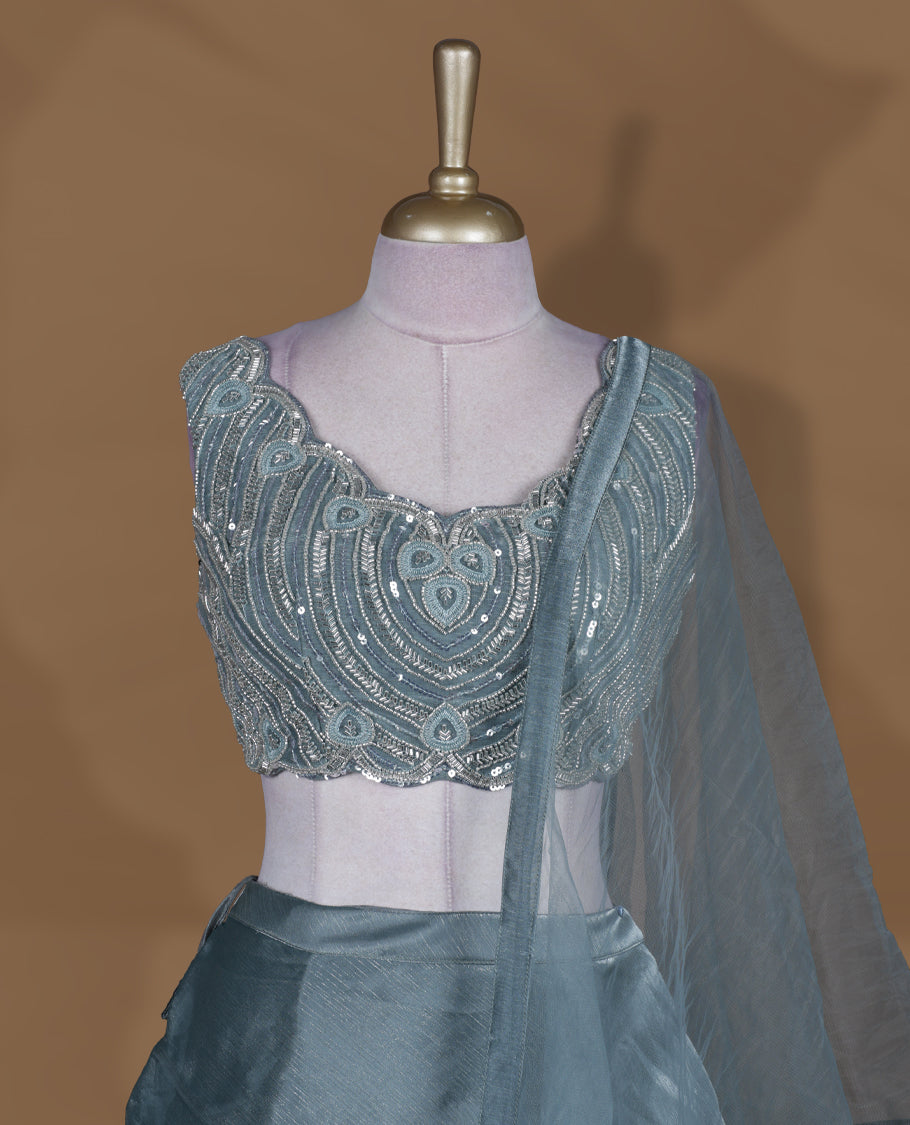 Dusty teal blue colour lehenga set with stitched sleeveless heavily embellished blouse featuring scalloped neckline, matching stitched flared lehenga, and plain sheer dupatta.