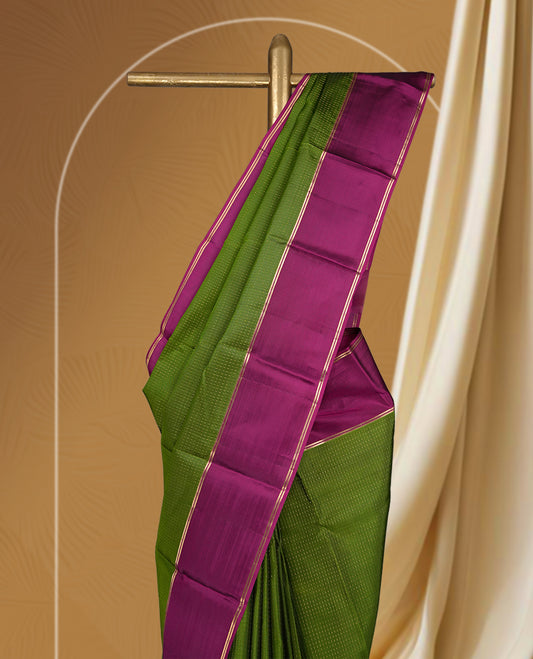 Leaf green colour soft silk saree adorned with intricate self striped, enhanced by a vibrant magenta pink zari border and pallu with rich detailing & paired with a matching blouse.