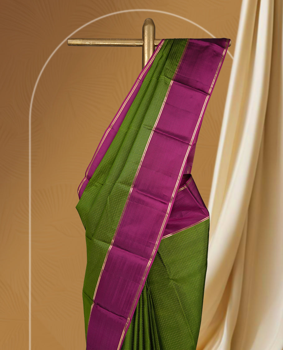 Leaf green colour soft silk saree adorned with intricate self striped, enhanced by a vibrant magenta pink zari border and pallu with rich detailing & paired with a matching blouse.