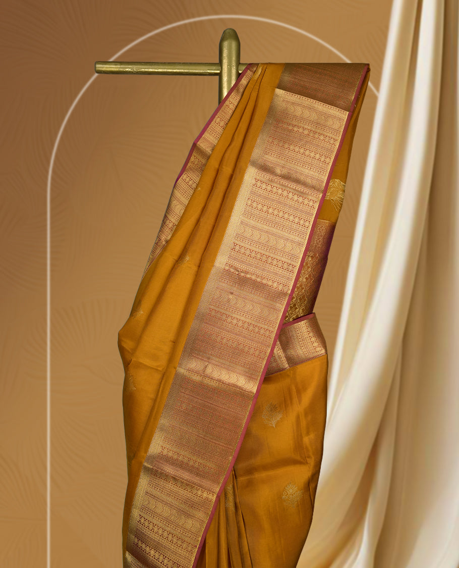 Ochre yellow colour soft silk saree adorned with small golden buttas, enhanced by a rich gold zari border and pallu with intricate detailing & paired with a matching blouse.