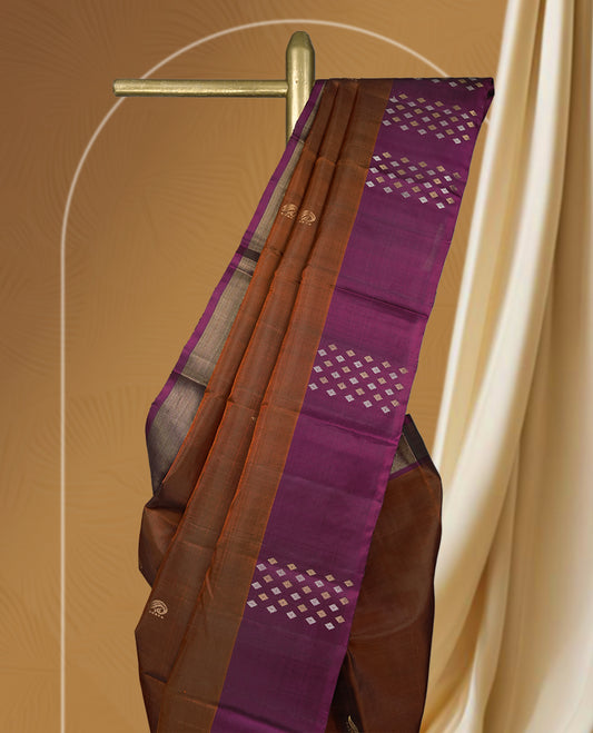 Brown colour soft silk saree adorned with tiny golden buttas, complemented by a rich purple border and pallu with elegant zari designs & Paired with a matching blouse.