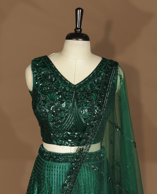 Emerald green colour lehenga set with stitched sleeveless V‑neck heavily sequinned blouse featuring cut‑out tie‑up back, matching stitched flared lehenga, and net dupatta with sequin border and scattered floral motifs.