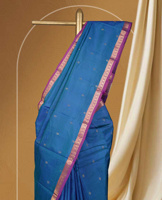 Blue colour soft silk saree adorned with delicate zari buttas, complemented by a rich contrast purple border with intricate golden zari work & Paired with a matching blouse.