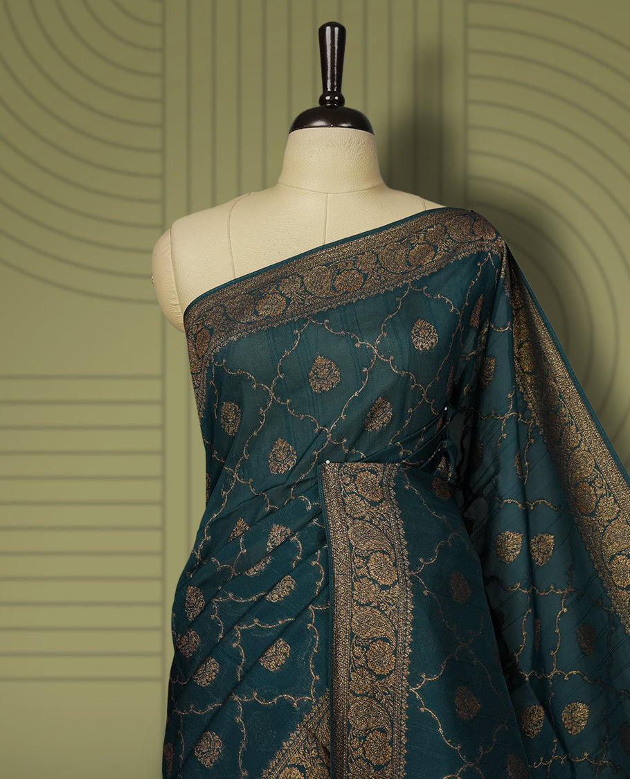 Deep peacock blue colour semi Banarasi Tussar Georgette saree with gold zari motifs on the body, a grand woven golden pallu, and ornate zari border. Includes a matching blouse piece for a complete look.