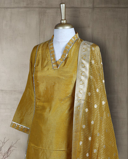 Golden yellow salwar from TWARA, featuring a V neck with delicate sequin highlights and plain finish on the top, paired with a matching bottom and a rich Banarasi style dupatta adorned with zari motifs and a contrast border.