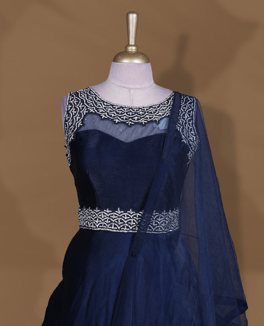 Navy blue colour Gown with stitched sleeveless embellished blouse featuring sheer yoke and waist detailing, matching stitched flared lehenga with tassel accents, and plain sheer dupatta.