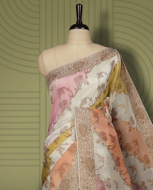Pastel cream colour semi Banarasi Tussar Georgette saree with soft peach, lilac, and sage yellow floral motifs, antique gold zari border, and intricately woven pallu. Comes with matching blouse piece.