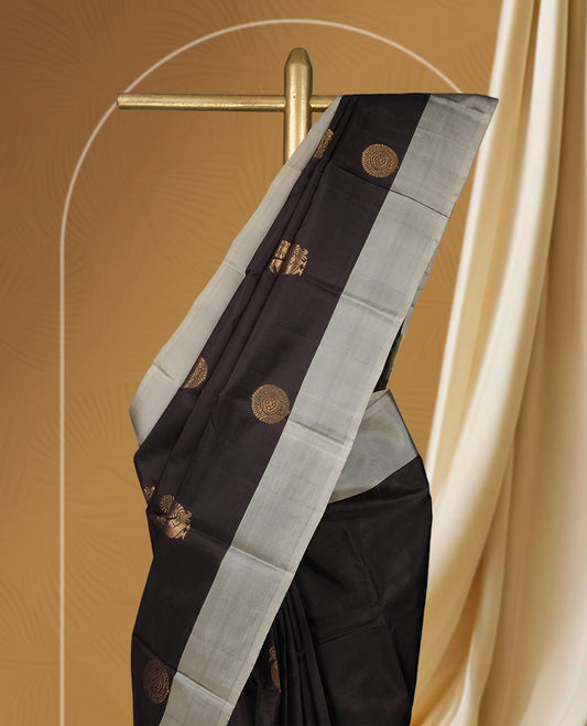 Dark brown colour soft silk saree embellished with graceful golden buttas, enhanced by an elegant silver grey border and pallu & Paired with a matching blouse.