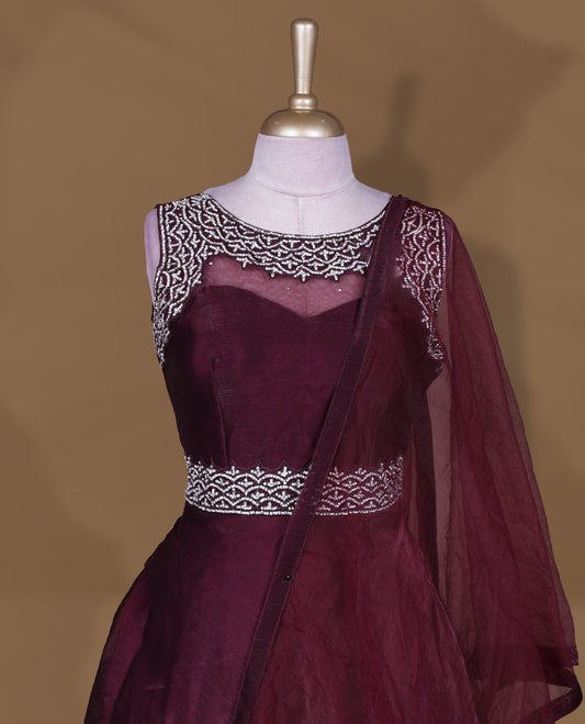 Wine colour Gown with stitched sleeveless embellished blouse featuring sheer yoke and waist detailing, matching stitched flared lehenga, and plain sheer dupatta.