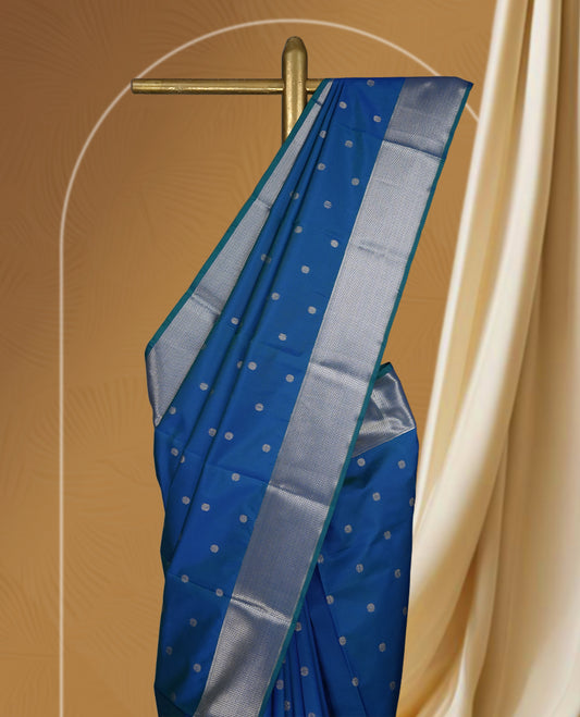 Royal blue colour soft silk saree adorned with small silver buttas, enhanced by a shimmering silver zari border and pallu with delicate motifs & paired with a matching blouse.