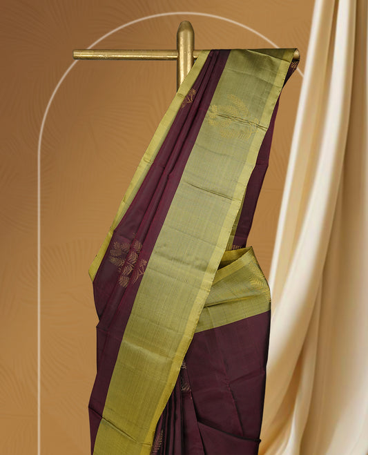 Maroon colour soft silk saree adorned with small golden buttas, enhanced by a shimmering light olive green zari border and pallu with delicate motifs & paired with a matching blouse.