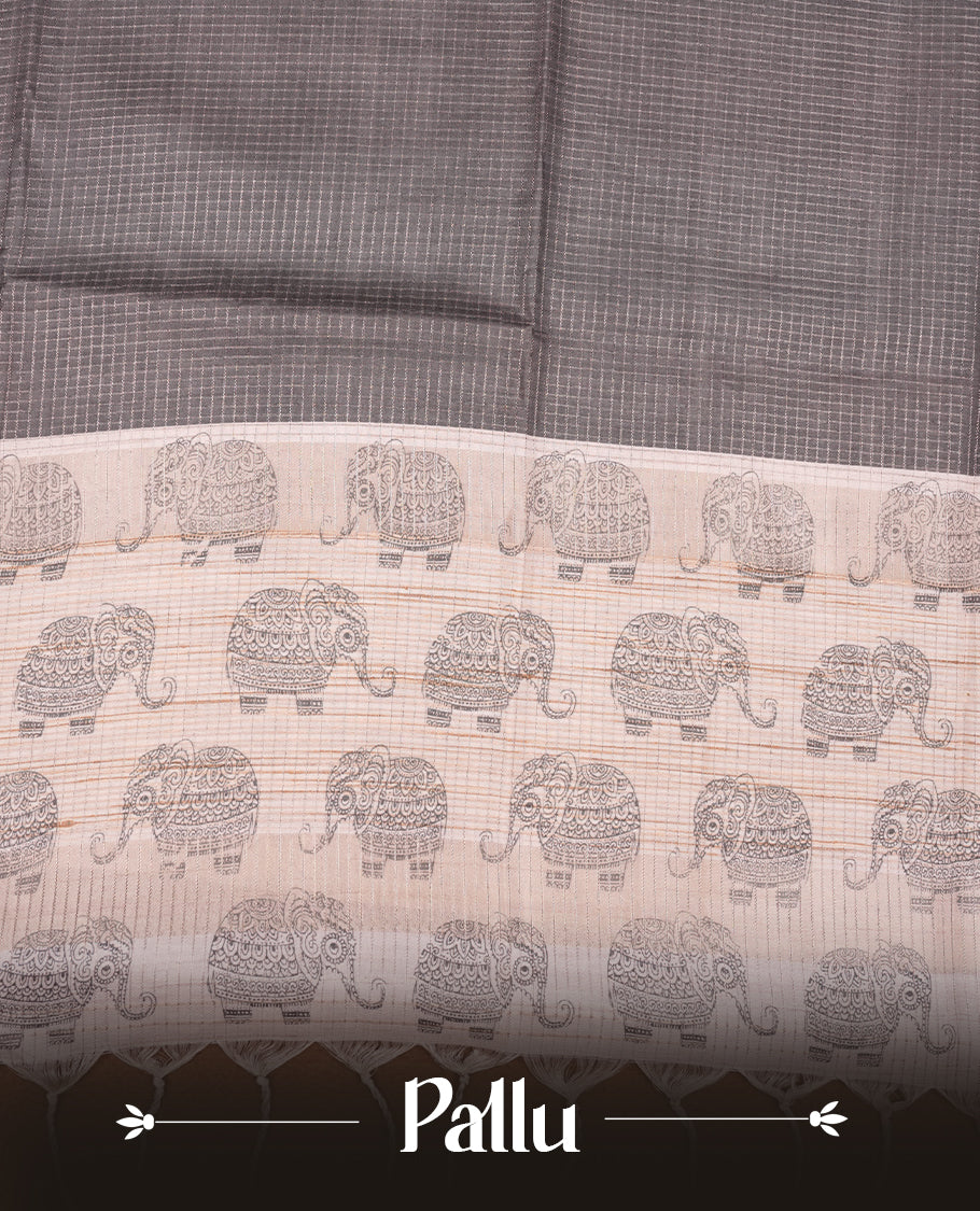 Charcoal green colour semi tussar silk saree featuring an all-over elephant motif print across the body, complemented by a contrasting blue pallu and border, and paired with a matching blouse piece.