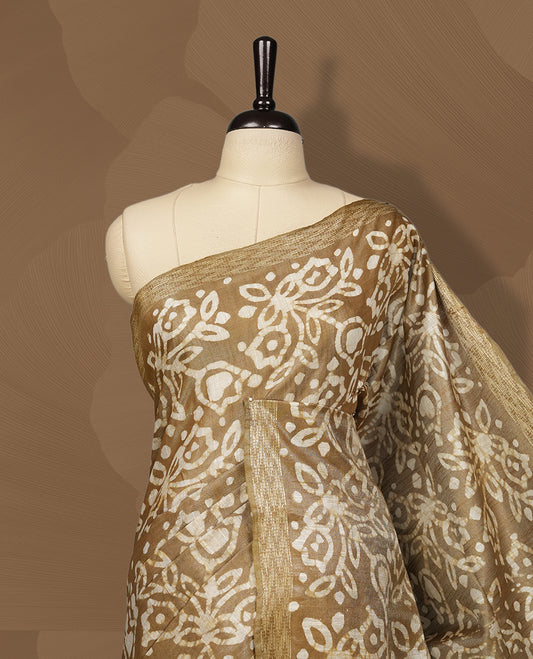 Golden brown semi jute tissue saree featuring elegant floral motifs all over the body, complemented by a shimmering zari striped pallu, woven golden border, and matching blouse piece for a graceful look.