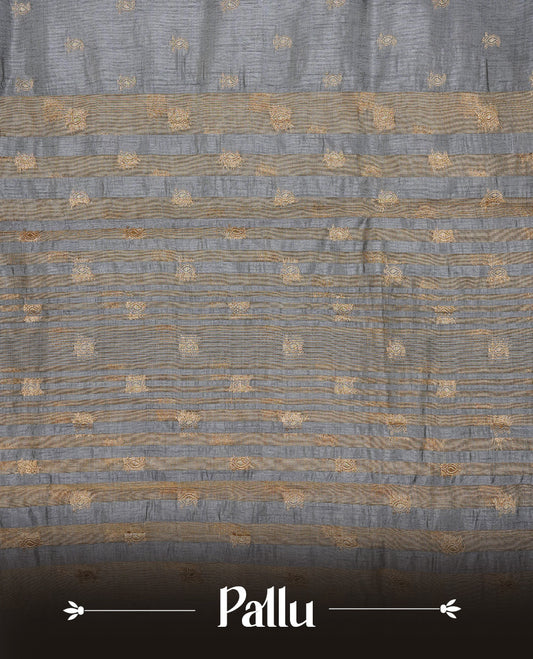 Grey colour semi tussar silk saree featuring small gold zari mango motifs across the body, enhanced with a self colour border showcasing elegant gold zari mango patterns. Paired with a matching blouse piece.