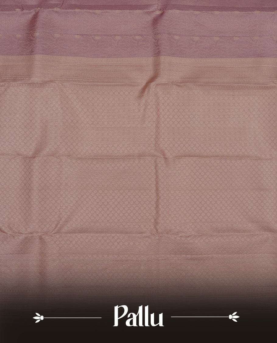 Dusty lavender colour Vasundhara silk saree adorned with all-over self color leaf kodi motifs on the body, complemented by a self colour with gold line pattern border and paired with a matching blouse piece.