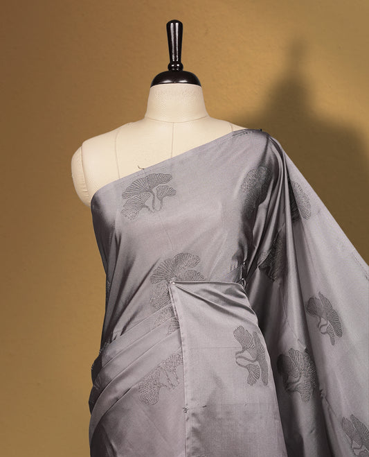 Grey colour semi soft silk saree featuring intricate woven floral motifs on the body, complemented by a rich woven border and pallu with tassel finish & Comes with a matching blouse piece for an elegant look.
