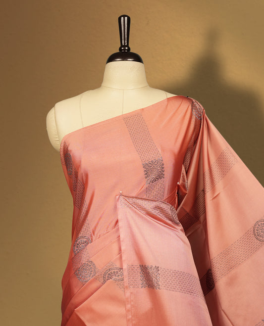 Amber rose colour semi soft silk saree, adorned with subtle self woven motifs on the body & The design is elevated with an elegant zari border & pallu with intricate detailing and tassel accents, paired with a matching blouse.