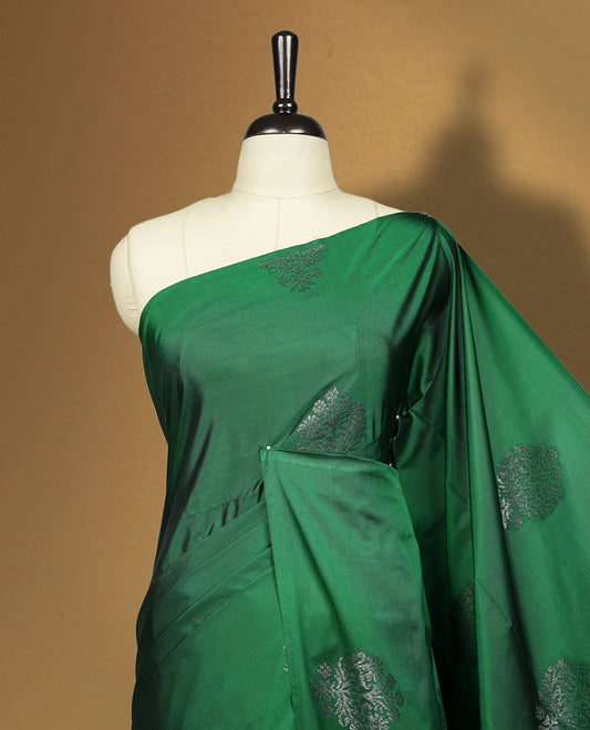 Royal Green colour semi soft silk saree adorned with delicate woven floral motifs on the body, complemented by a rich contrast woven pallu with intricate detailing and tassel accents & Comes with a matching blouse piece.
