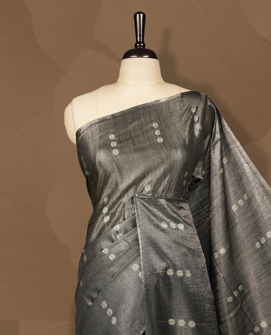 Grey colour semi jute tissue saree accentuated with subtle dotted motifs across the body, The saree features a finely woven pallu and sleek borders, adding a touch of understated elegance & Comes with a matching blouse piece.