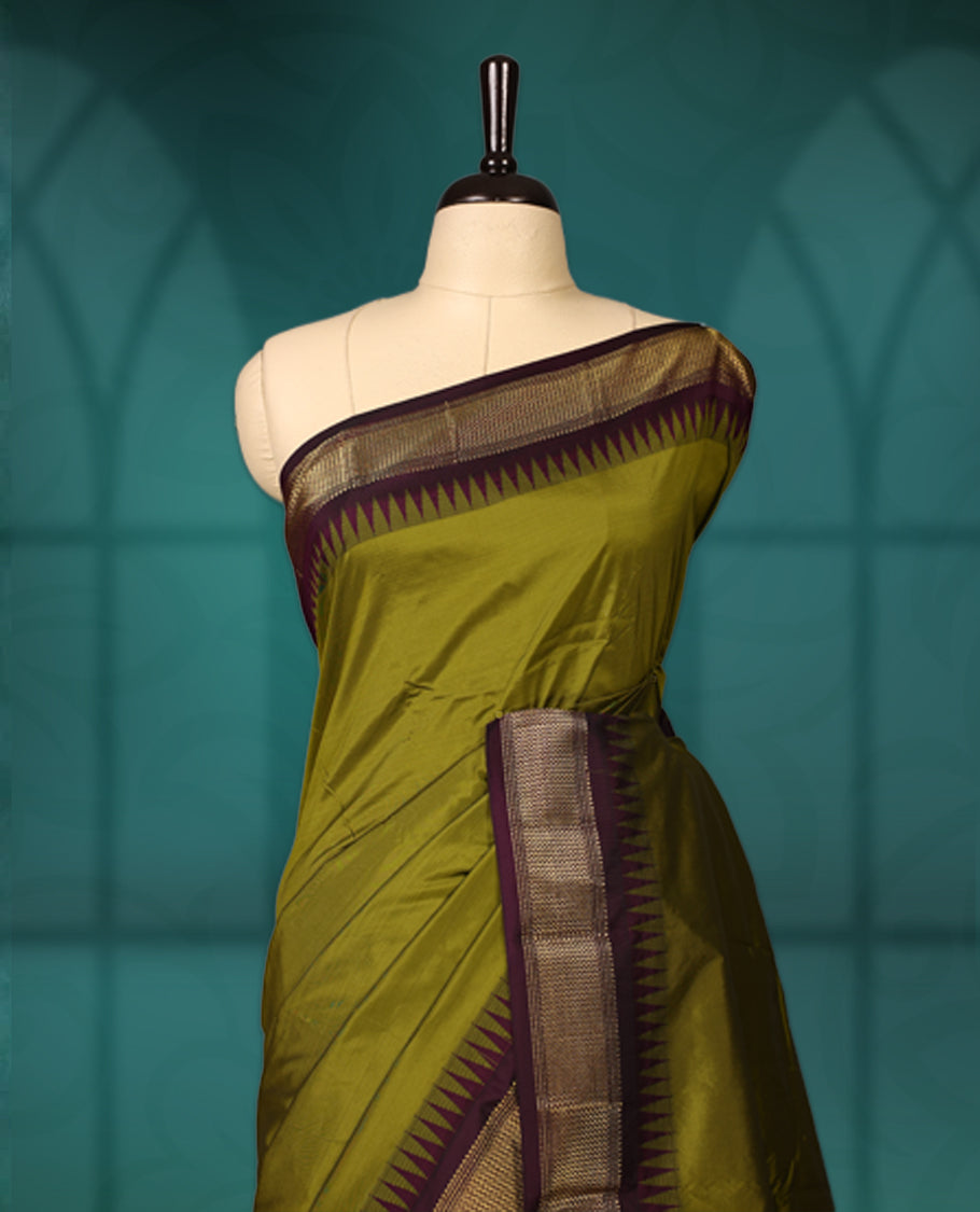 Olive green semi silk saree with plain body, vibrant deep purple pallu and matching purple border adorned with golden zari, accented with temple motifs along the edges, Paired with a matching blouse, perfect for festive occasions.