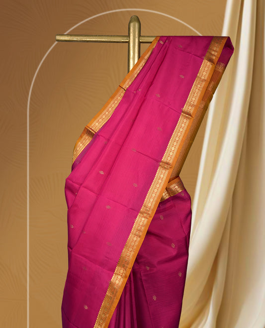 Magenta colour soft silk saree with golden buttas, enhanced by a vibrant orange zari border and pallu, paired with a matching blouse.