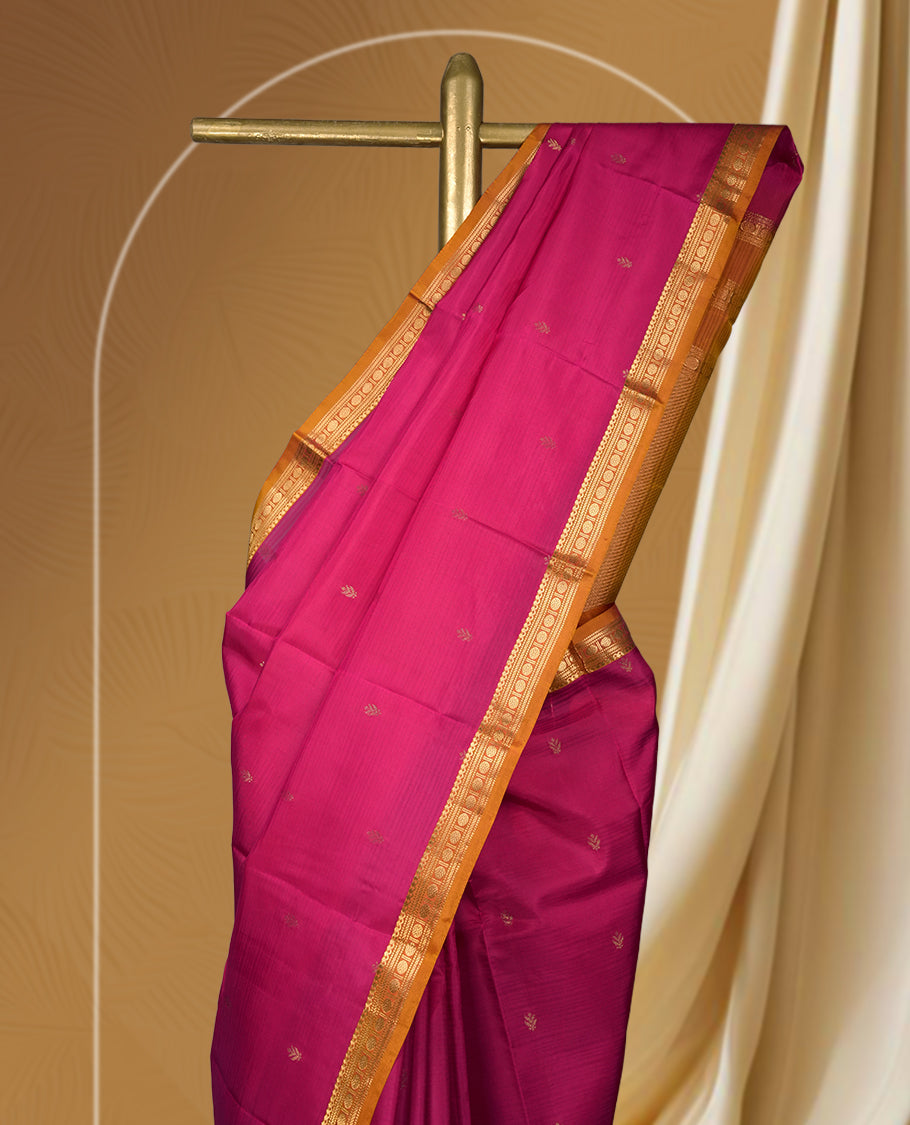 Magenta colour soft silk saree with golden buttas, enhanced by a vibrant orange zari border and pallu, paired with a matching blouse.