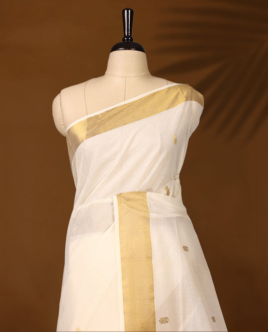 Traditional Kerala Kasavu saree in ivory with golden zari paisley motifs and a rich pallu, The graceful drape is perfect for festivals and weddings, Style with gold accessories for an elegant ethnic look.