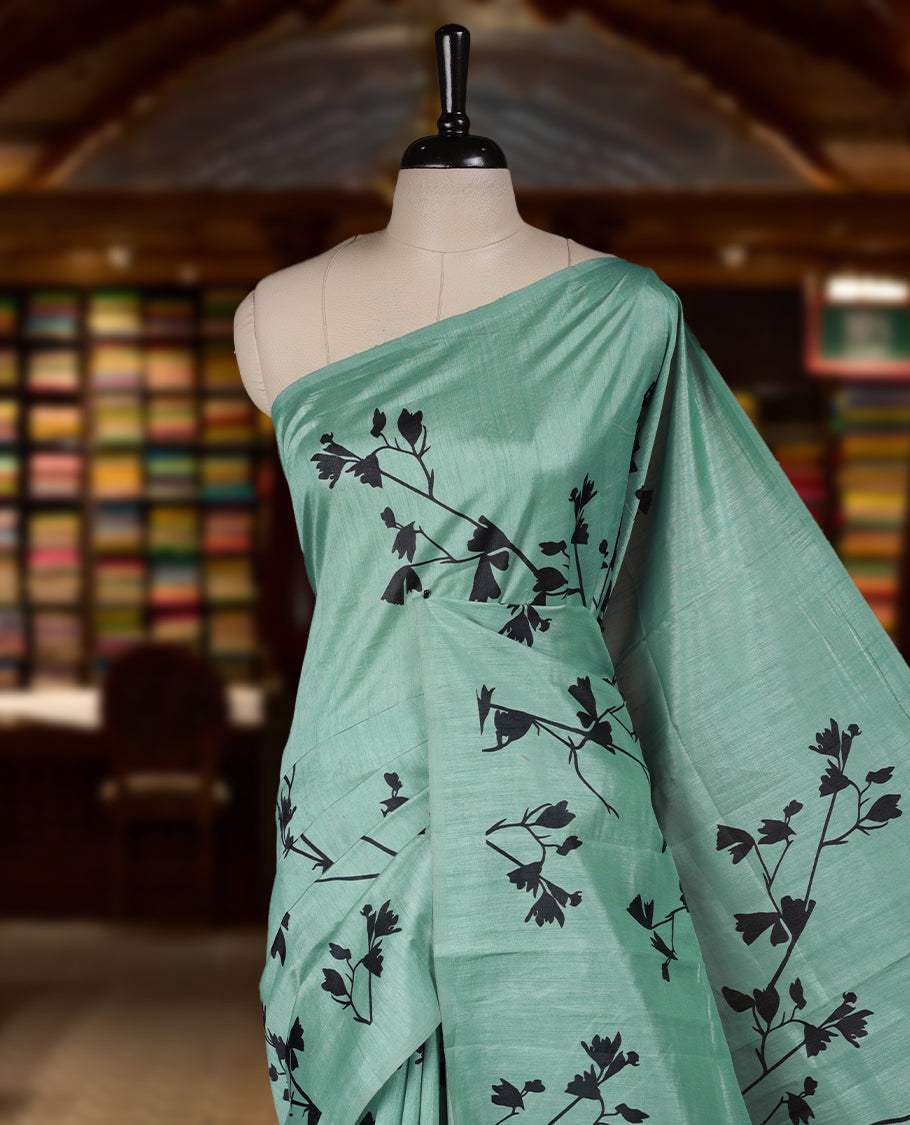 Pastel Green colour Semi tussar silk saree adorned with black floral prints on the body and an elegant pallu & Comes with a matching blouse piece for a classy look.