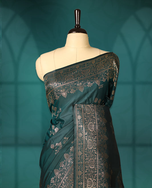 Teal green colour semi silk saree featuring elegant silver zari floral motifs across the body, complemented by a rich self-colour woven border and pallu, paired with a matching blouse.