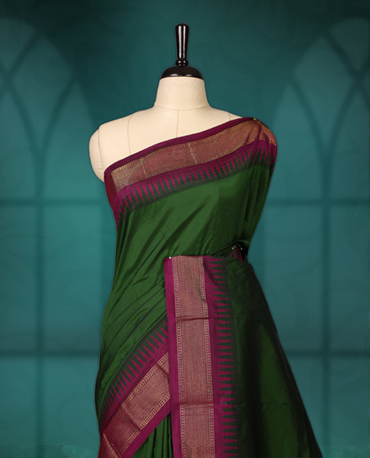 Deep green semi silk saree with plain body, vibrant deep magenta pallu and matching magenta border adorned with golden zari, accented with temple motifs along the edges, Paired with a matching blouse, perfect for festive occasions.