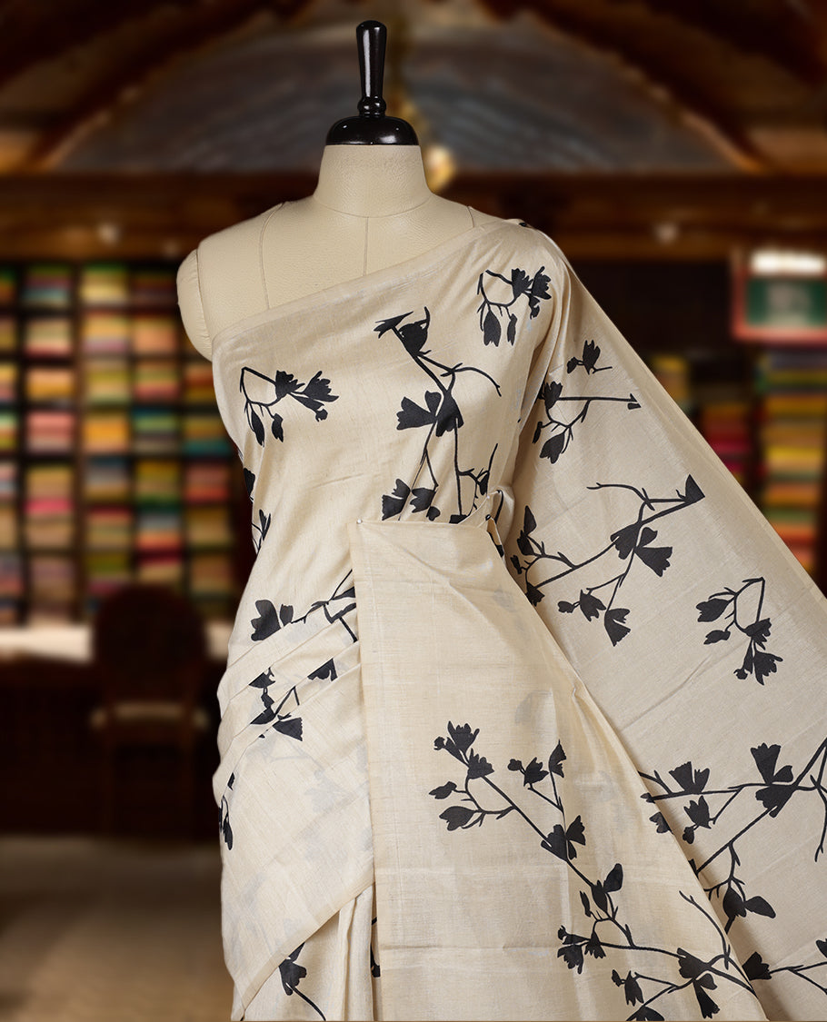 Pastel Ivory colour Semi tussar silk saree adorned with black floral prints on the body and an elegant pallu & Comes with a matching blouse piece for a classy look.