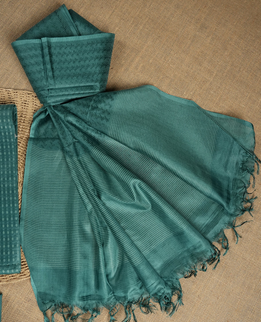 Teal blue colour tussar suit material featuring a subtle self woven textured body, paired with a soft striped dupatta detailed with tassel edges and a matching bottom piece.