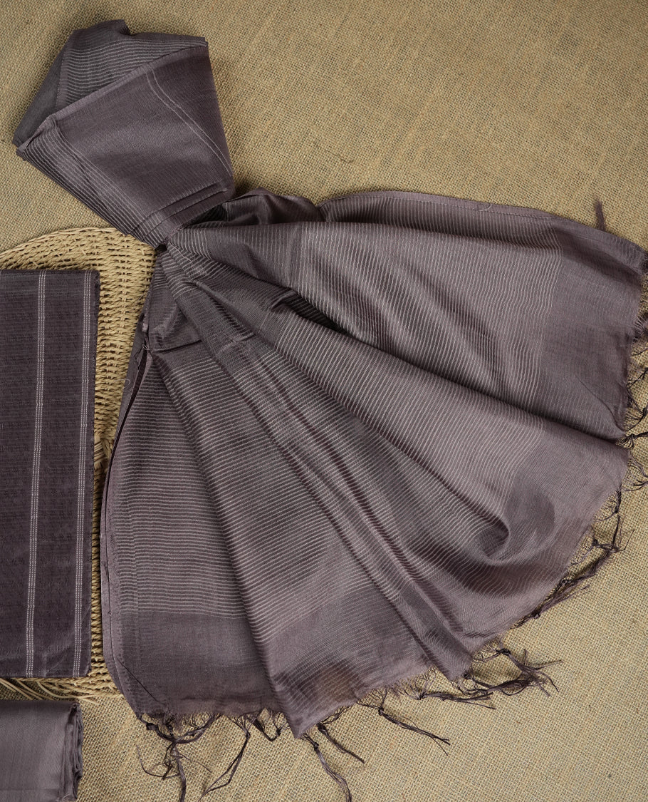 Dark pastel purple colour tussar suit material featuring a subtle self woven pattern and vertical lines on the body, paired with a lightweight matching dupatta with tassel edges and a plain bottom piece.