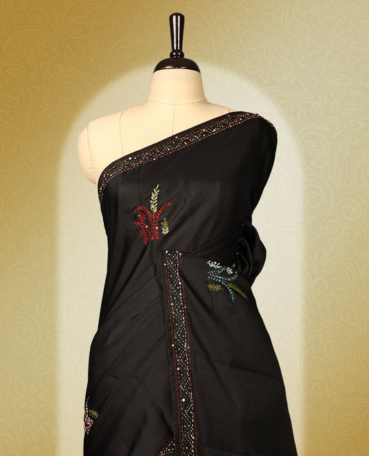 Black colour pure tussar saree adorned with delicate multicolour floral embroidery along the border and scattered motifs across the body, paired with a matching blouse.