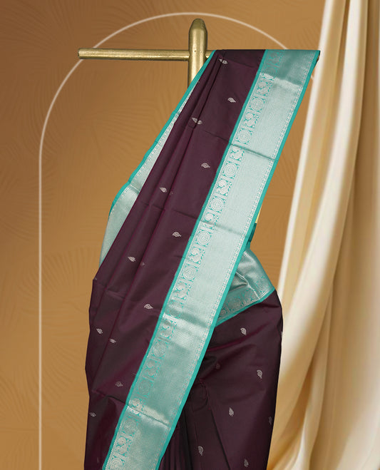 Deep plum colour body soft silk saree adorned with silver buttas, paired with a contrasting light aqua green zari border & Comes with a matching blouse.