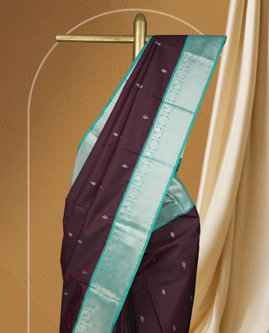 Deep plum colour body soft silk saree adorned with silver buttas, paired with a contrasting light aqua green zari border & Comes with a matching blouse.