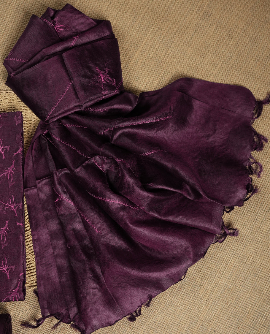 Dark grape colour tussar suit material featuring elegant floral thread embroidery on the body, paired with a soft dupatta adorned with matching embroidered motifs and tassel edges, along with a plain bottom piece.