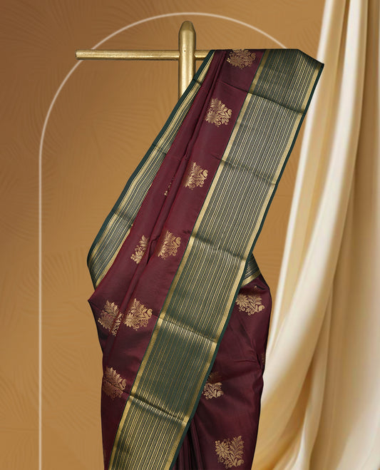Deep maroon colour soft silk saree adorned with golden buttas, enhanced by a striking green zari border and pallu with intricate designs & Paired with a matching blouse.