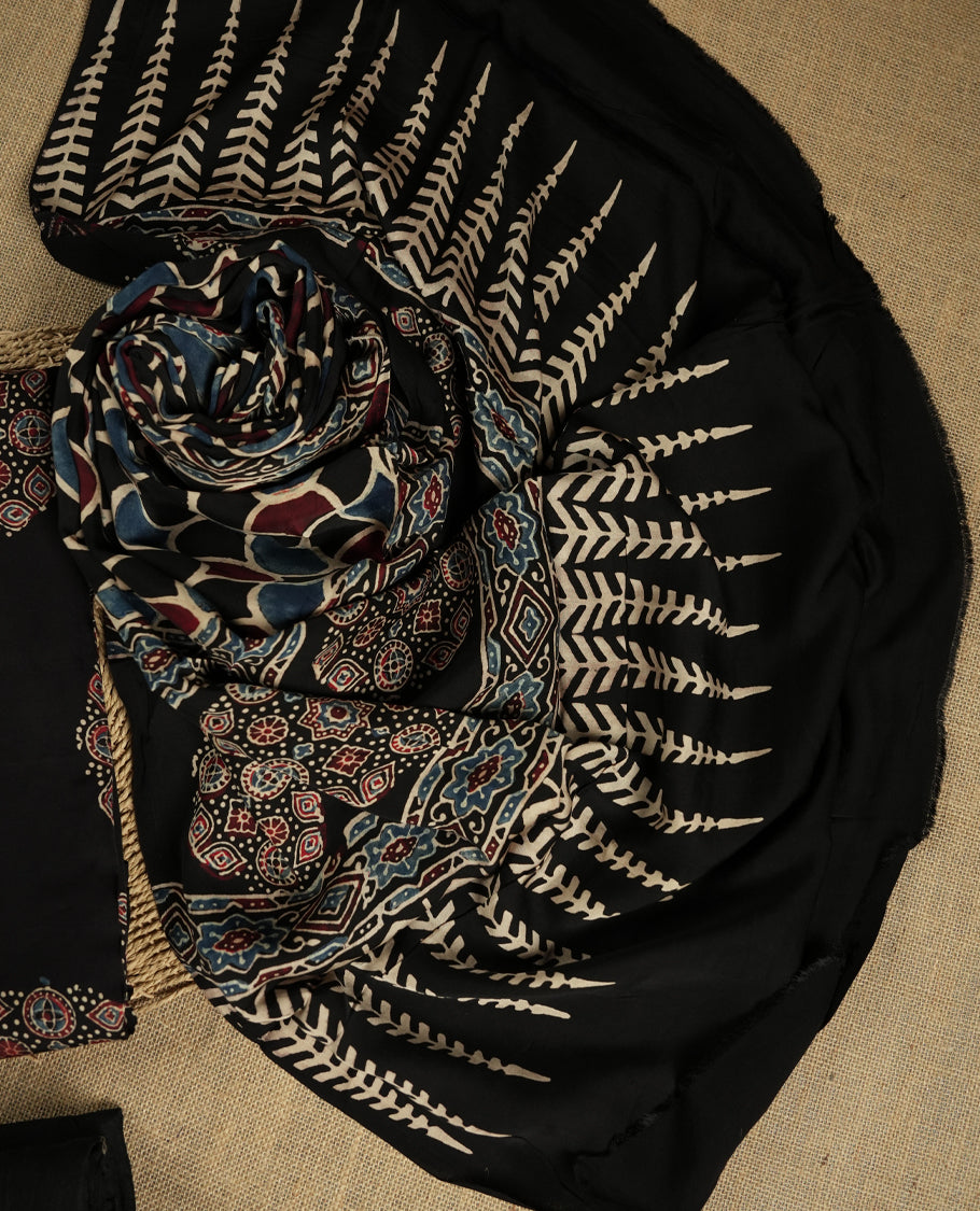 Black suit material featuring intricate Ajrak inspired prints in maroon, blue, and beige & Includes a beautifully patterned dupatta and matching plain bottom.